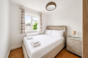 Un dormitorio con cama, una mesita de noche con lámpara, ventana con cortinas y vistas al exterior.