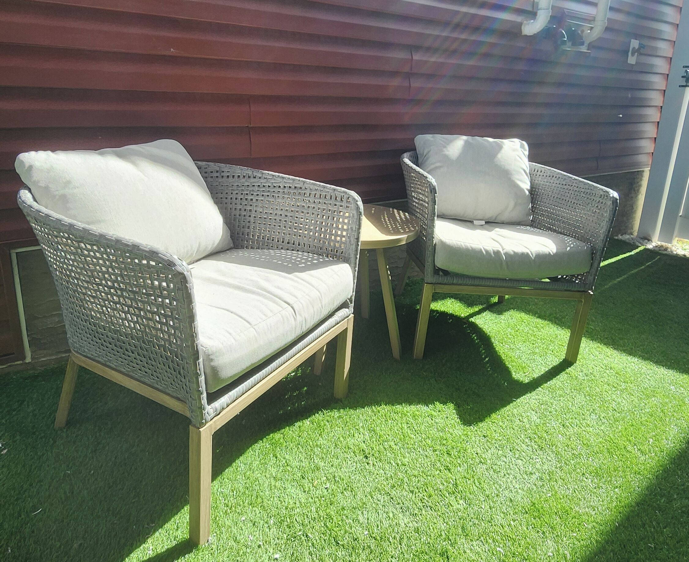 Two wicker chairs with cushions, a small round table, and artificial green grass.
