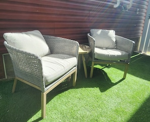 Two wicker chairs with cushions, a small round table, and artificial green grass. - Modern Suite in Seton - King Bed, 85" TV, Near South Health Campus & YMCA (Calgary)