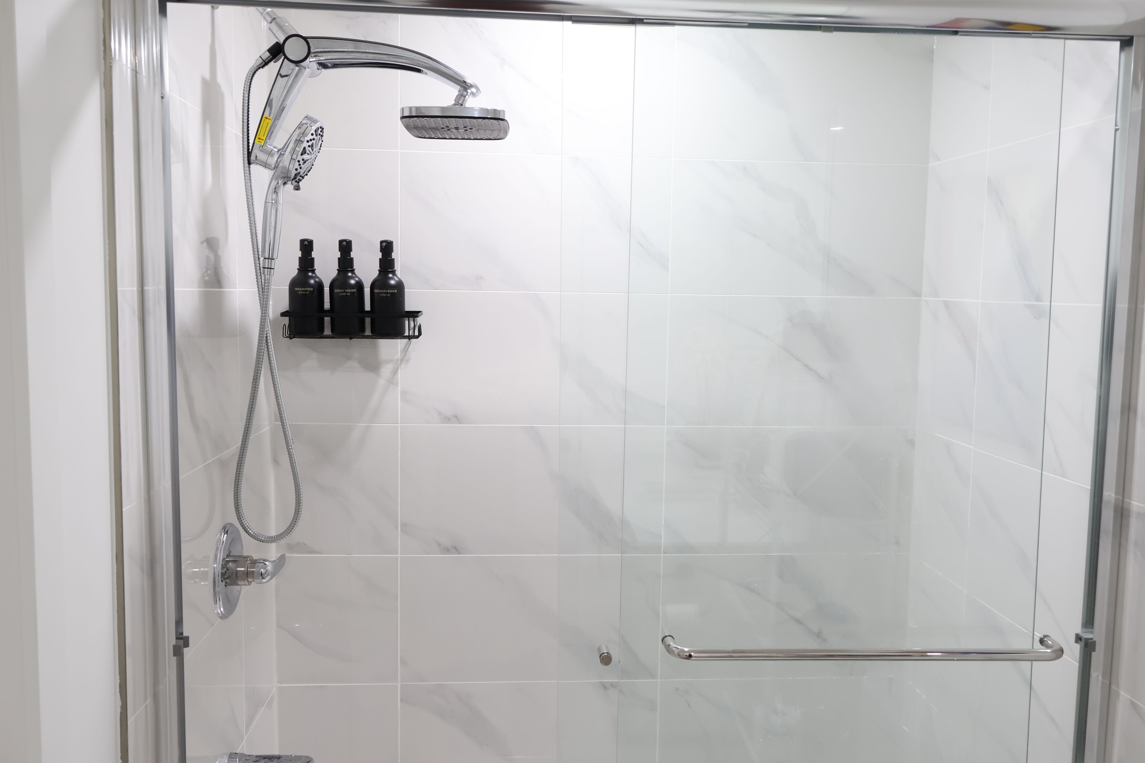 A glass-enclosed shower with a handheld showerhead and a handheld shower attachment.