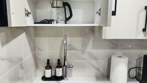 Un baño con lavamanos, cafetera y dos botellas de jabón.