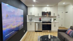 Una cocina moderna con electrodomésticos de acero inoxidable, un televisor de pantalla plana y una sala de estar con sofá y mesa de centro.