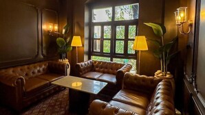 Une pièce faiblement éclairée, dotée d’une grande fenêtre, de canapés en cuir, d’une table basse et de lampes fixées au mur.