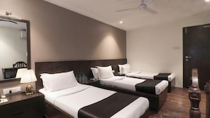 Une chambre d’hôtel avec trois lits, un grand miroir, un ventilateur de plafond et un plancher en bois.
