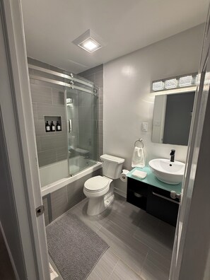 A modern bathroom with a glass-enclosed shower, a toilet, and a sink with a mirror above. -  3-bedroom house 5 minutes away from the beach  in Hampton Bays (Hampton Bays)