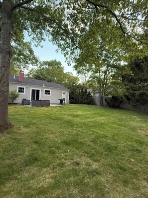 A residential backyard with a house, a tree, and a grassy lawn. -  3-bedroom house 5 minutes away from the beach  in Hampton Bays (Hampton Bays)