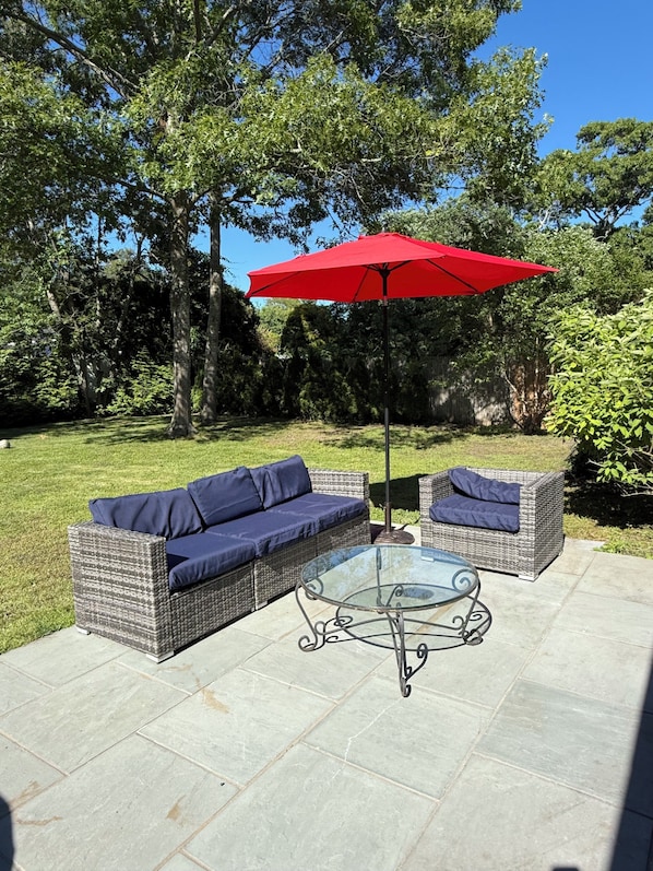 A patio with wicker furniture, a glass table, and a red umbrella. - 3-bedroom house 5 minutes away from the beach in Hampton Bays (Hampton Bays)