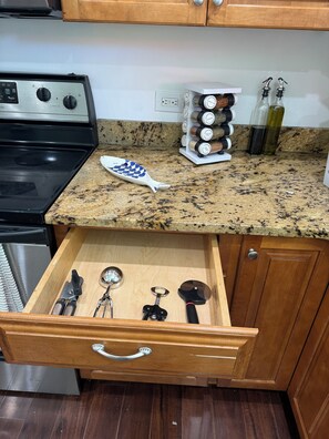 A kitchen with a granite countertop, a fish-shaped salt shaker, a spice rack, and a drawer with kitchen utensils. - 3-bedroom house 5 minutes away from the beach in Hampton Bays (Hampton Bays)