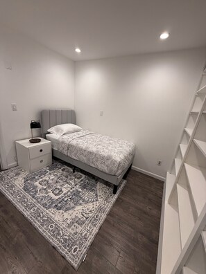 A bedroom with a bed, nightstand, and a patterned rug. -  3-bedroom house 5 minutes away from the beach  in Hampton Bays (Hampton Bays)