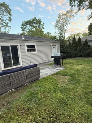 Ein Garten mit Haus, Grill, überdachter Sitzgruppe und Rasenfläche.
