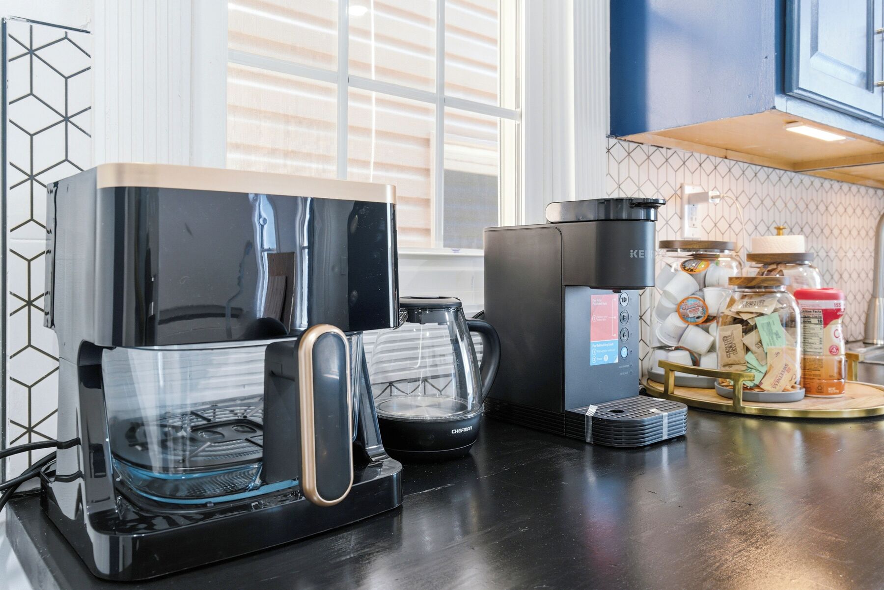 A kitchen with a coffee maker, a kettle, and a coffee machine.