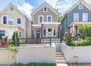A row of townhouses with a central entrance, a covered porch, and a small garden area. - 3BR Passaic Home Near NY/NJ Stadium, NYC Access, Sleeps 6 (Passaic)