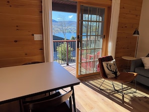 Ein Holzinnenraum mit Tisch, Stuhl, Sofa und Seeblick durch eine Glastür.