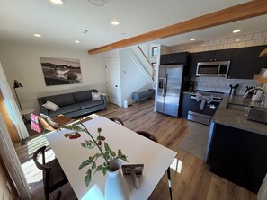 A modern kitchen with stainless steel appliances, a dining area with a white table, and a grey sofa.