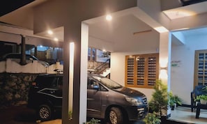 A modern building with a covered parking area, a staircase, and a seating area with plants.