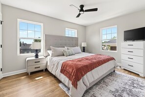 Une chambre à coucher avec un lit, des tables de chevet, un ventilateur de plafond, une télévision et une fenêtre.