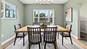A dining room with a wooden table, black chairs, a chandelier, and a large window with a view of the outside. - Fully Updated Field Club Colonial - 4BR Near UNMC & Blackstone (Omaha)
