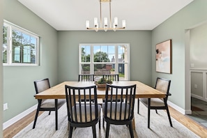 A dining room with a wooden table, black chairs, a chandelier, and a large window with a view of the outside. - Fully Updated Field Club Colonial - 4BR Near UNMC & Blackstone (Omaha)