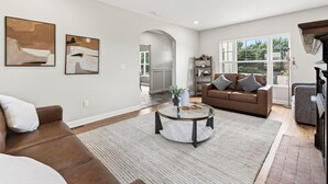 A spacious living room with a brown leather sofa, a round coffee table, and two abstract paintings on the wall. - Fully Updated Field Club Colonial - 4BR Near UNMC & Blackstone (Omaha)