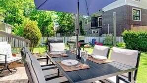 An outdoor patio with a table set for dining, surrounded by chairs, and a large umbrella providing shade. - Elevated French‑country coastal charm in the heart of Charlottetown (Charlottetown)