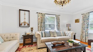 A living room with a sofa, a coffee table, a chandelier, and floral curtains. - Elevated French‑country coastal charm in the heart of Charlottetown (Charlottetown)
