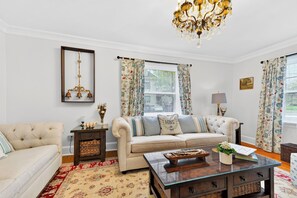 Una sala de estar con un sofá, una mesa de centro, una araña y cortinas con motivos florales.