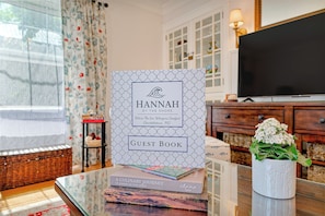 Ein Gästebuch mit dem Titel 'Hannah am Strand' in einem Zimmer mit Fernseher, Korbmöbeln und einer Vase mit Blumen.
