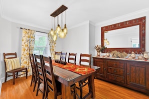 A dining room with a wooden table, chairs, a chandelier, and a large mirror.