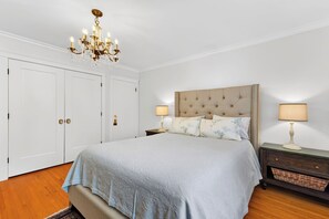 Un dormitorio con una cama grande, dos mesitas de noche con lámparas, una araña y un armario.