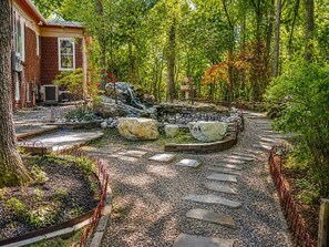 Ein Gartenpfad mit trittfesten Steinen, ein kleiner Wasserfall und ein Backsteinhaus mit Klimaanlage.