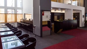 Een moderne hotel lobby met een lange receptiebalie, meerdere zithoeken en grote ramen.