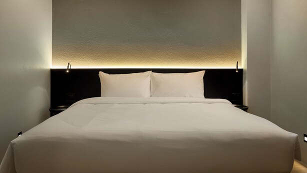 Een opgemaakt bed met witte lakens in een hotelkamer.