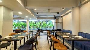 Een restaurant met tafels en stoelen klaar voor dineren, een zwembad zichtbaar door de ramen en een modern interieur.