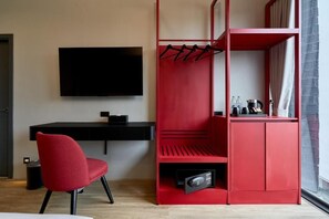 A modern room with a black desk, a red chair, a TV mounted on the wall, and a red storage unit with a hanging rack. - Lantern Chiang Mai Night Bazaar Hotel (Chiang Mai)