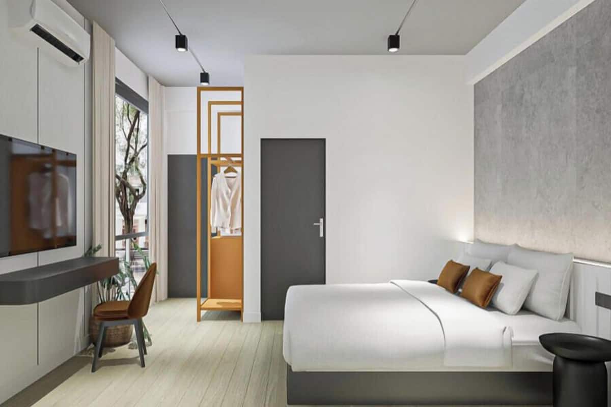 A modern hotel room with a bed, a desk, a chair, a wardrobe, and a television.