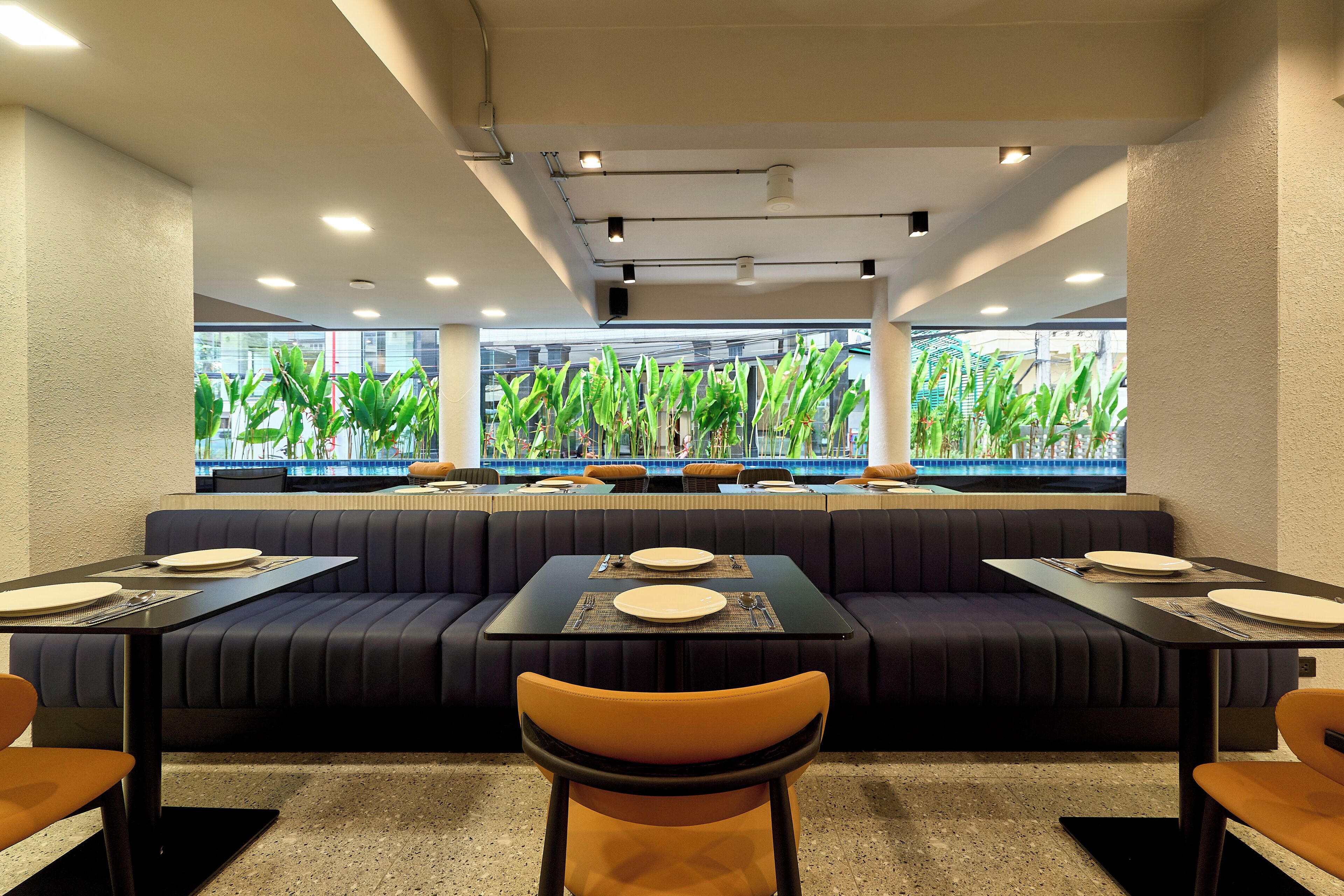 A restaurant with a long counter, booths, and a view of greenery through large windows.