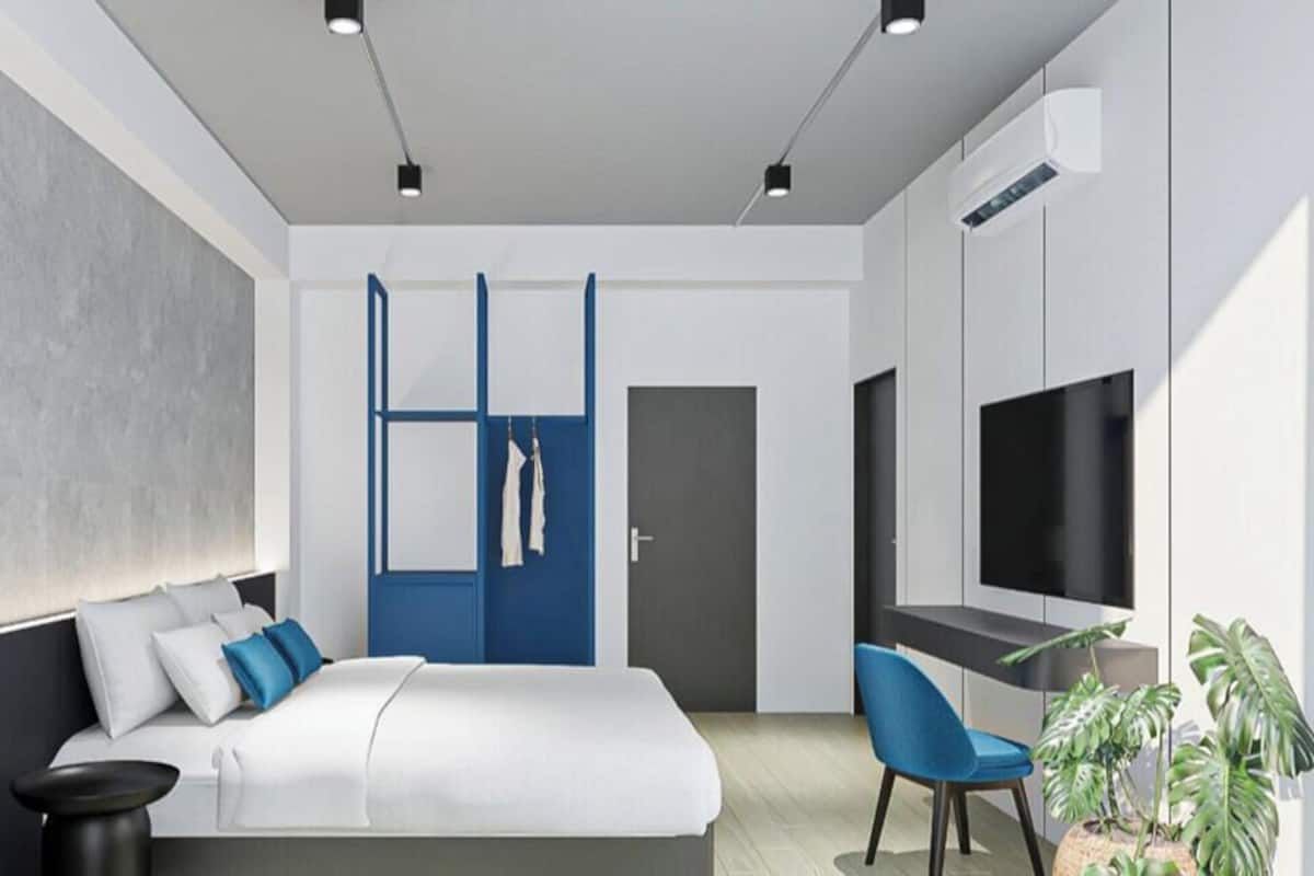 A modern hotel room with a bed, a desk, a chair, a TV, and a plant.