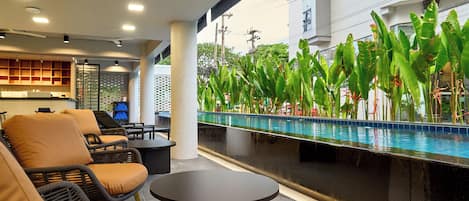 A poolside area with lounge chairs, a bar, and a view of a building with a pool.