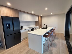 Eine moderne Küche mit einer zentralen Kochinsel, Barhocker und einem schwarzen Kühlschrank.