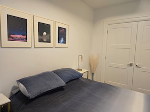 Une chambre à coucher avec un lit, une table de chevet, une lampe, une porte et trois tableaux encadrés accrochés au mur.