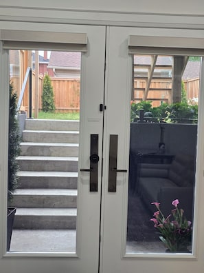 Un ensemble composé de deux portes doubles blanches à mécanisme coulissant, d’un petit espace extérieur délimité par une clôture en bois et d’un escalier en béton menant à l’extérieur.