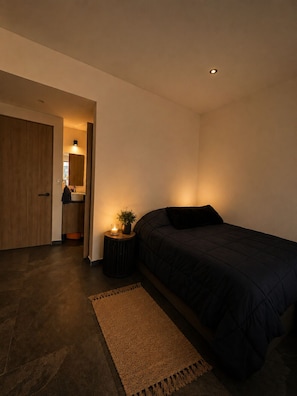 Ein Schlafzimmer mit einem Bett, einem Nachttisch mit einer Kerze, einem Teppich und einer Tür zu einem Badezimmer.