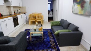Un espace de vie compact comprenant un canapé, une table basse, une table à manger avec des chaises, un lave-linge et un coin cuisine.
