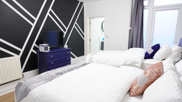Une chambre d’hôtel avec deux lits, un téléviseur à écran plat posé sur une commode et une fenêtre avec des rideaux.