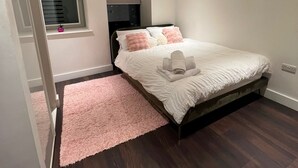 Een slaapkamer met een bed, een raam met zonwering, een roze vloerkleed en een plafondlamp.