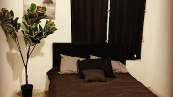 A bedroom with a bed, a potted plant, a window with curtains, and a wall-mounted painting.