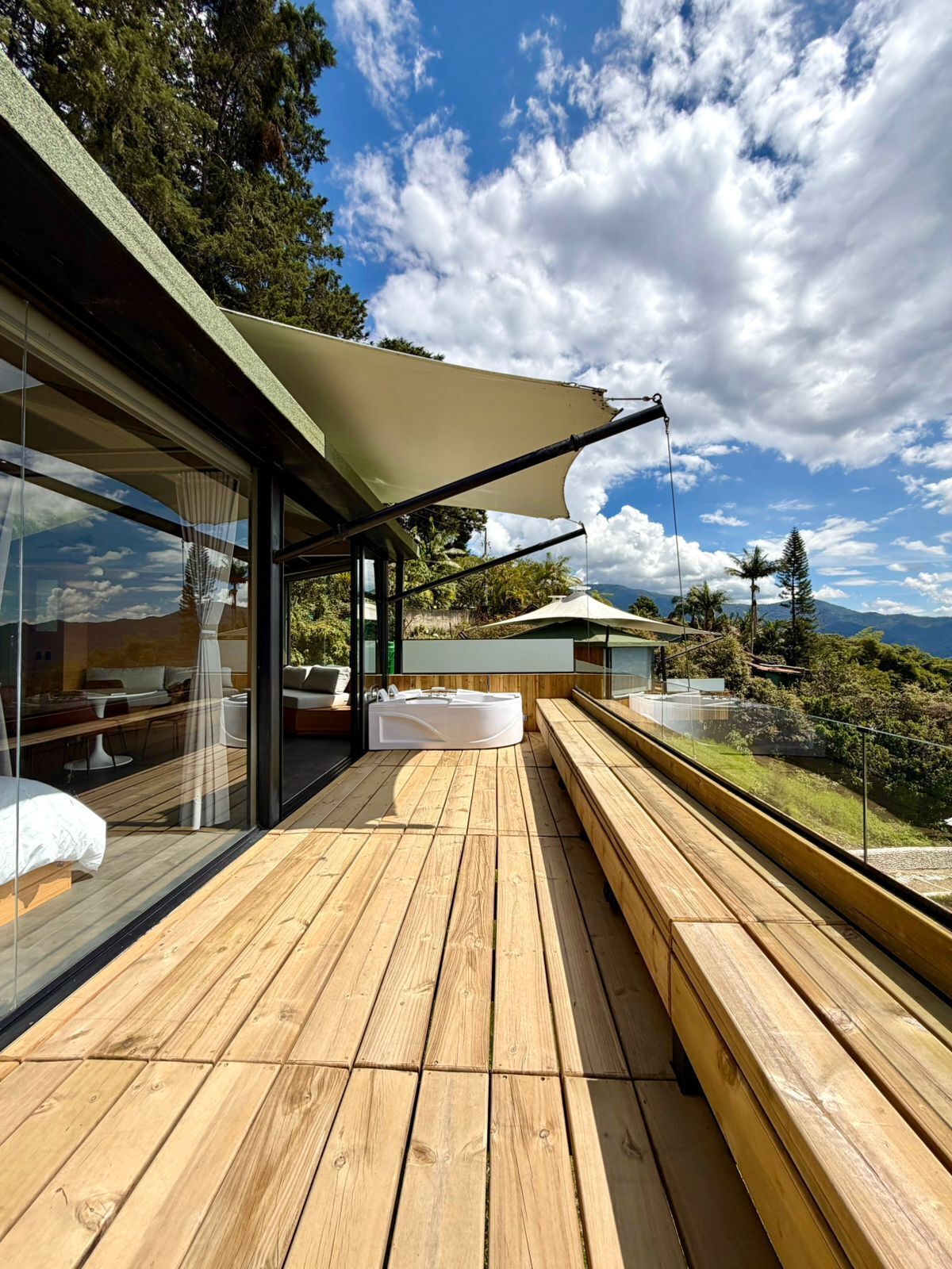 Una terrazza in legno con una vasca idromassaggio, area salotto all'aperto e un grande ombrellone per l'ombra.