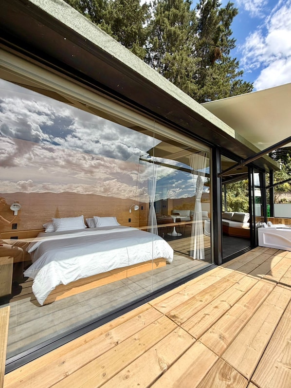 Une chambre moderne avec un grand lit, une porte vitrée donnant sur un espace extérieur et une vue sur le ciel par la fenêtre.