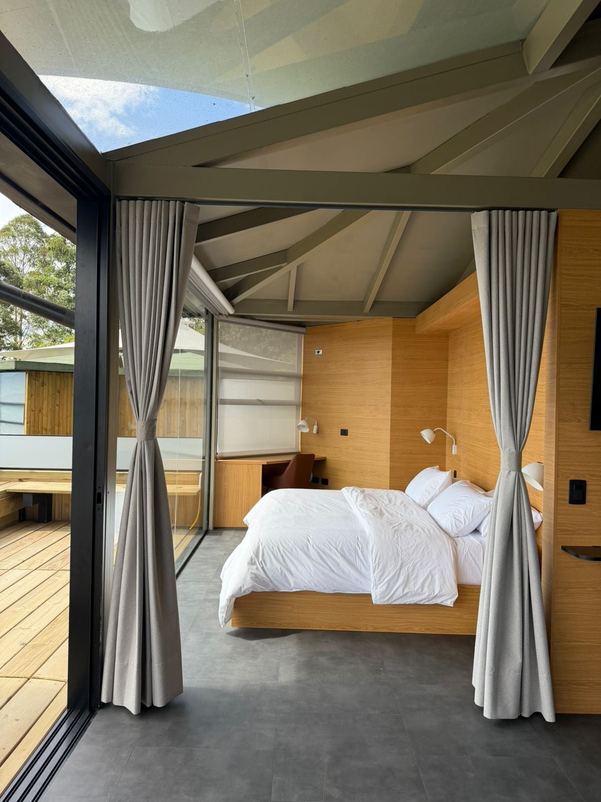 A modern bedroom with a bed, curtains, a desk, and a chair.