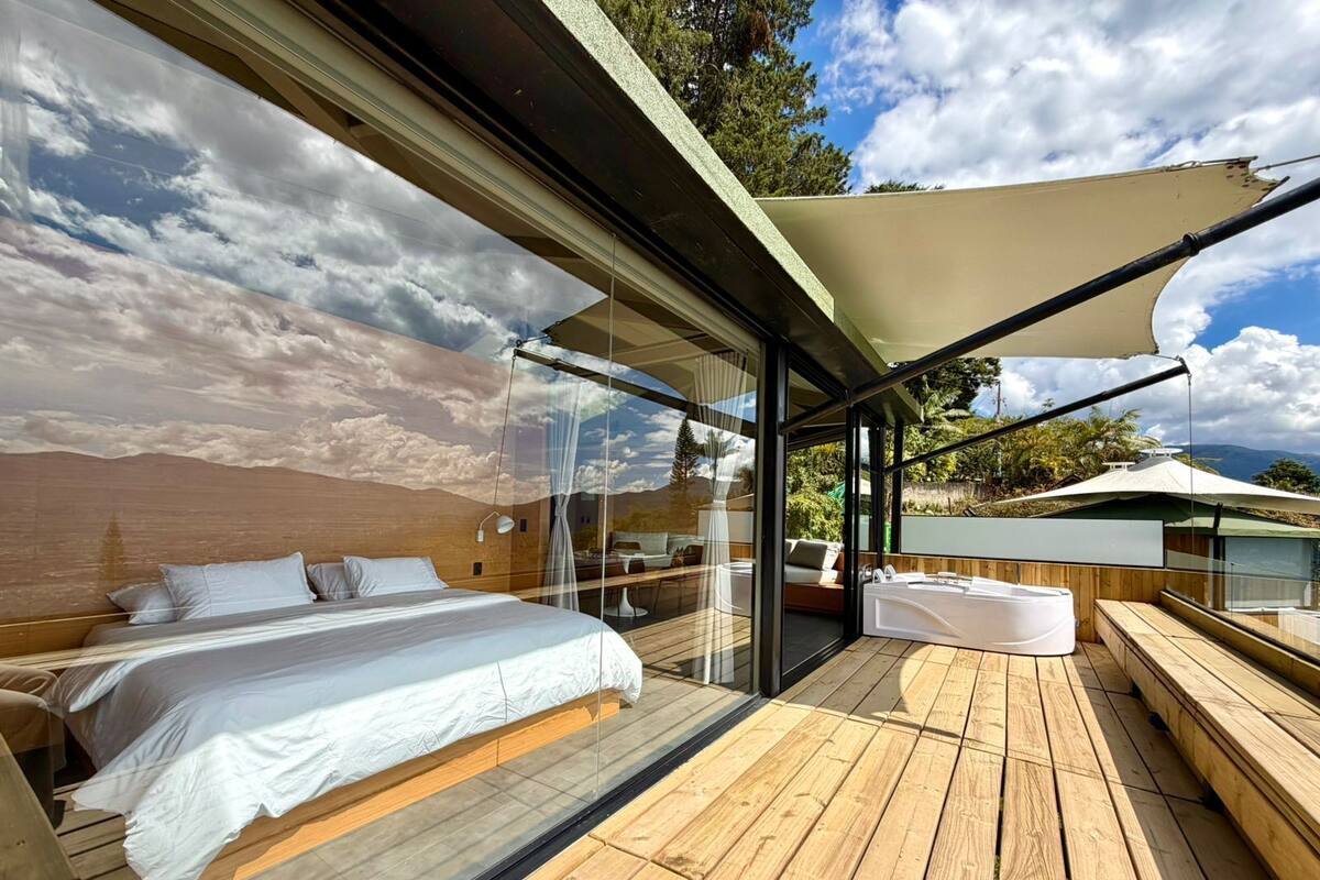 A modern bedroom with a large bed, a glass wall, and a wooden deck.